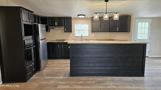 kitchen with a sink, light wood finished floors, a center island, under cabinet range hood, and black appliances