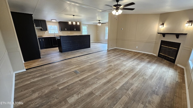 unfurnished living room with baseboards, wood finished floors, a glass covered fireplace, and a ceiling fan