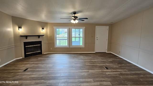 unfurnished living room featuring a glass covered fireplace, a decorative wall, visible vents, ceiling fan, and dark wood-type flooring