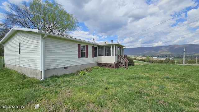 view of side of home with a lawn, a sunroom, a mountain view, and crawl space