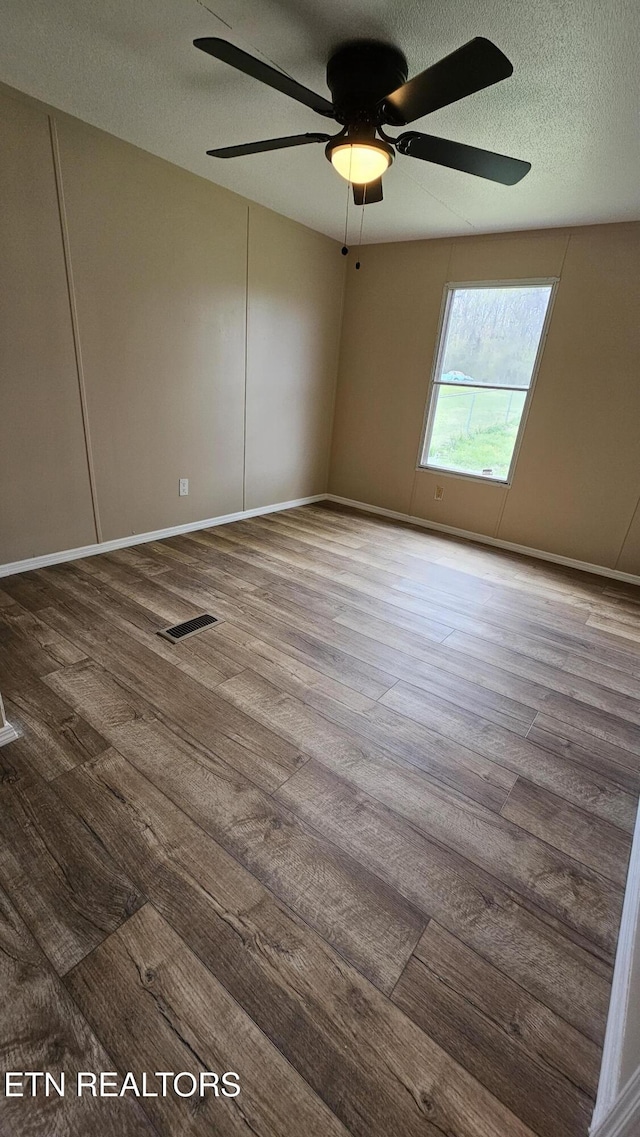 spare room featuring baseboards, a textured ceiling, visible vents, ceiling fan, and wood finished floors