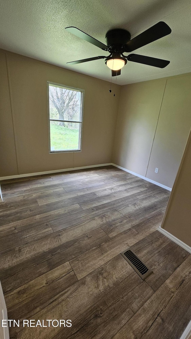 empty room with a textured ceiling, visible vents, a ceiling fan, and wood finished floors
