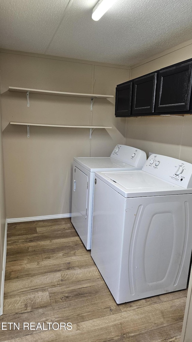 clothes washing area featuring washer and dryer, light wood-style flooring, cabinet space, and a textured ceiling