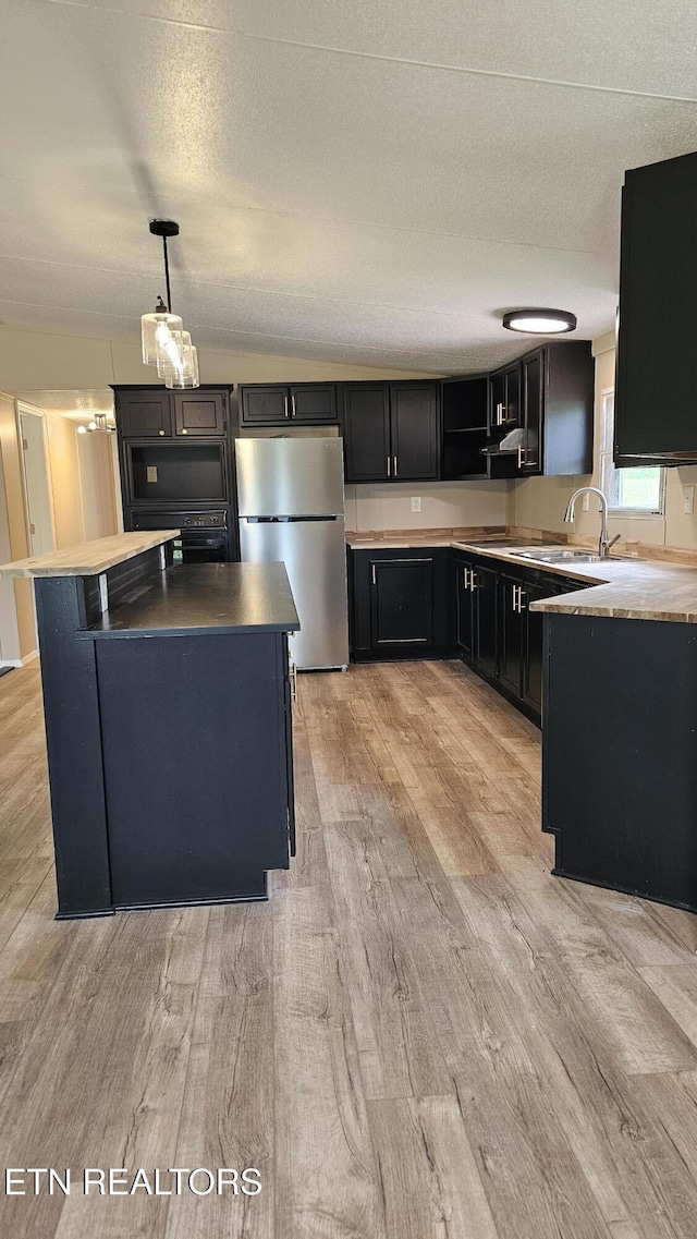 kitchen with a kitchen island, a sink, light wood-type flooring, dark cabinetry, and freestanding refrigerator