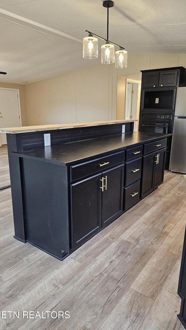 kitchen featuring dark countertops, light wood-style floors, dark cabinetry, and freestanding refrigerator