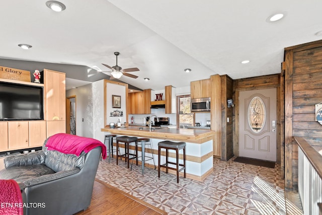 kitchen featuring a peninsula, ceiling fan, stainless steel microwave, a breakfast bar area, and vaulted ceiling