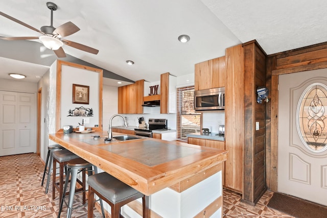 kitchen with ceiling fan, stainless steel appliances, a sink, vaulted ceiling, and a kitchen breakfast bar