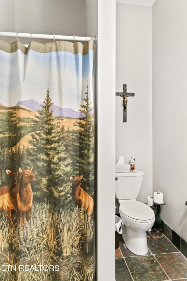 bathroom with baseboards, toilet, and stone tile floors