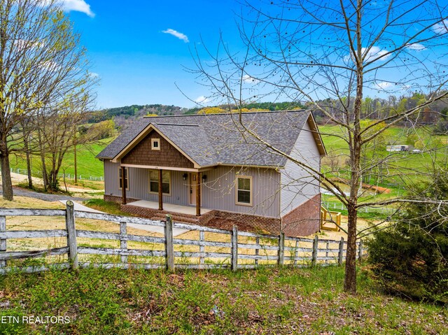 view of front of home with a shingled roof, a fenced front yard, and covered porch