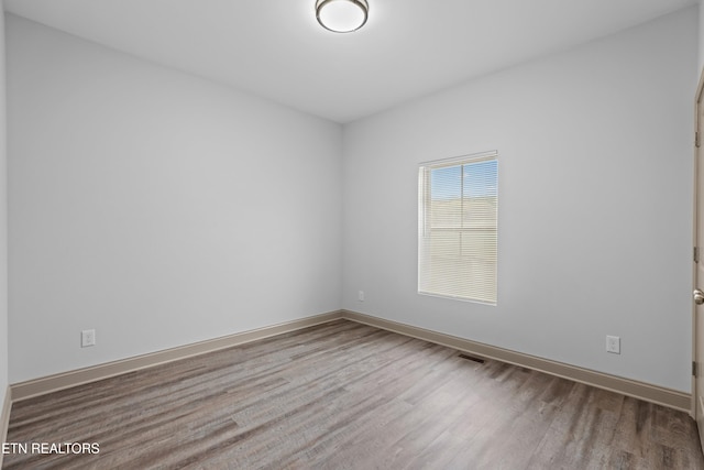 spare room with baseboards, visible vents, and wood finished floors