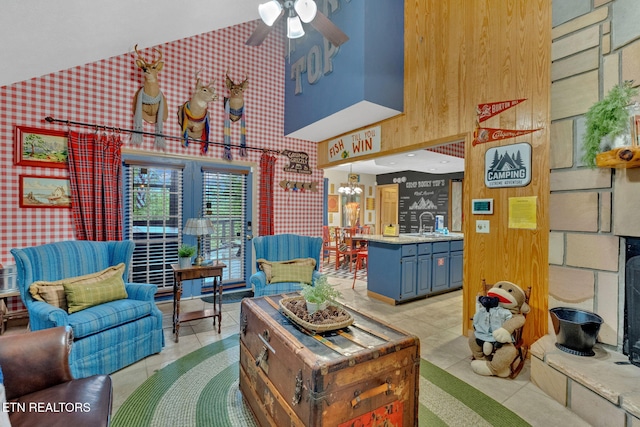 living room with high vaulted ceiling, light tile patterned floors, and ceiling fan with notable chandelier