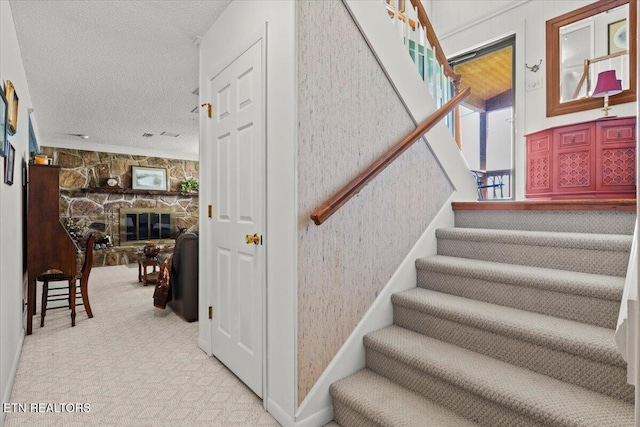 staircase with a textured ceiling, wallpapered walls, carpet flooring, and a fireplace