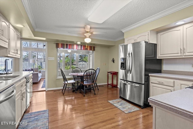 kitchen with light wood finished floors, crown molding, ceiling fan, and stainless steel appliances