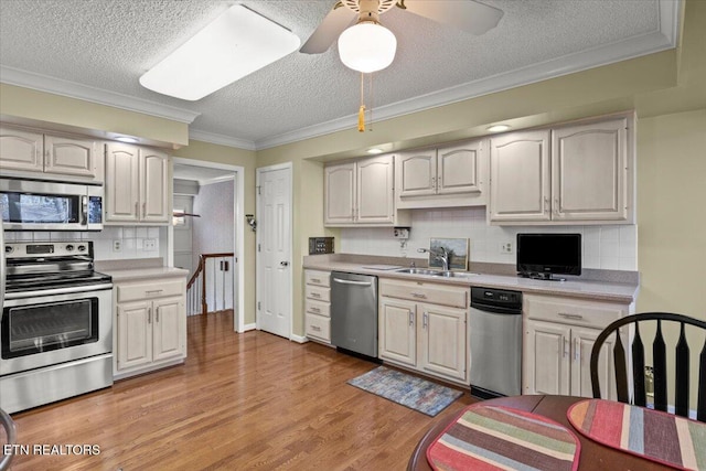 kitchen with ornamental molding, light countertops, light wood-style floors, appliances with stainless steel finishes, and a sink
