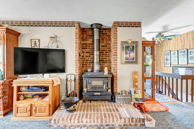 living area with a wood stove, a textured ceiling, and ceiling fan