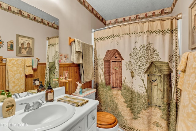 bathroom featuring a shower with shower curtain, toilet, a textured ceiling, vanity, and wainscoting