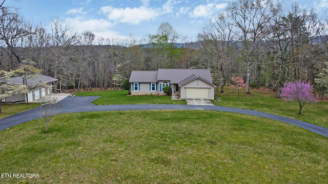 view of front of home featuring a wooded view, driveway, a front yard, and a garage