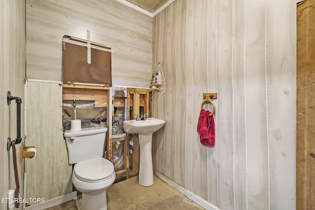 bathroom with toilet, wood walls, and a sink