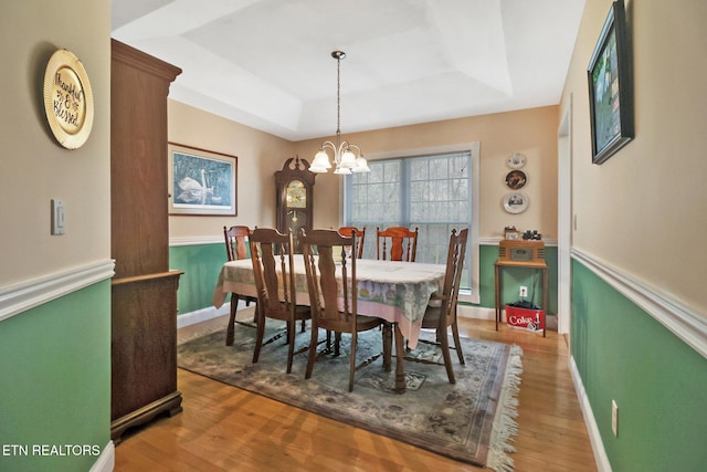 dining area featuring a raised ceiling, an inviting chandelier, and wood finished floors