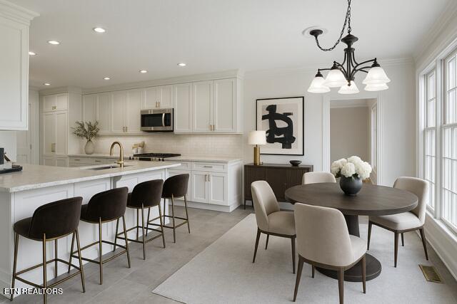 kitchen featuring a sink, stainless steel microwave, tasteful backsplash, an inviting chandelier, and light countertops