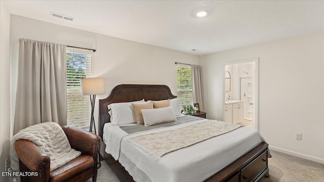 carpeted bedroom with baseboards, multiple windows, visible vents, and ensuite bath