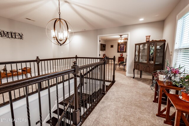 hall featuring an upstairs landing, a notable chandelier, visible vents, baseboards, and carpet floors