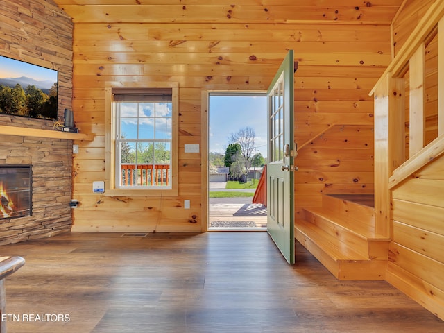 entrance foyer with visible vents, wood walls, a stone fireplace, and wood finished floors
