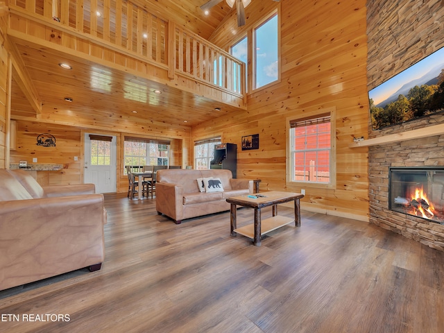 living room with a stone fireplace, wood walls, ceiling fan, wood ceiling, and wood finished floors