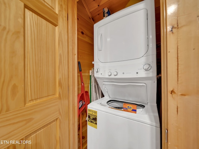 clothes washing area with laundry area, wooden walls, and stacked washer / drying machine