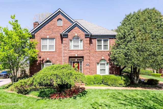 colonial inspired home with brick siding, a front lawn, roof with shingles, and a chimney