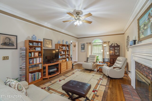living area featuring ornamental molding, a brick fireplace, wood finished floors, and ceiling fan