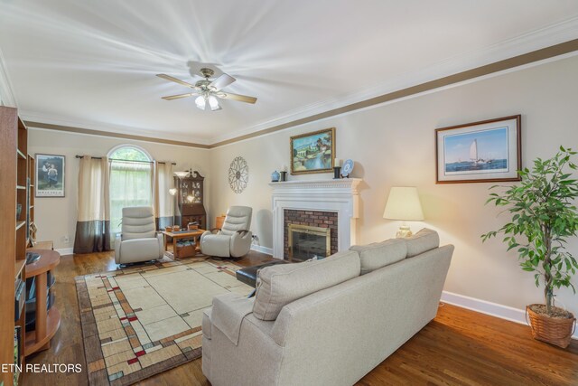 living room with ornamental molding, wood finished floors, a fireplace, baseboards, and a ceiling fan