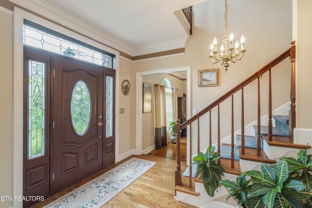 entrance foyer with a notable chandelier, ornamental molding, wood finished floors, and stairway