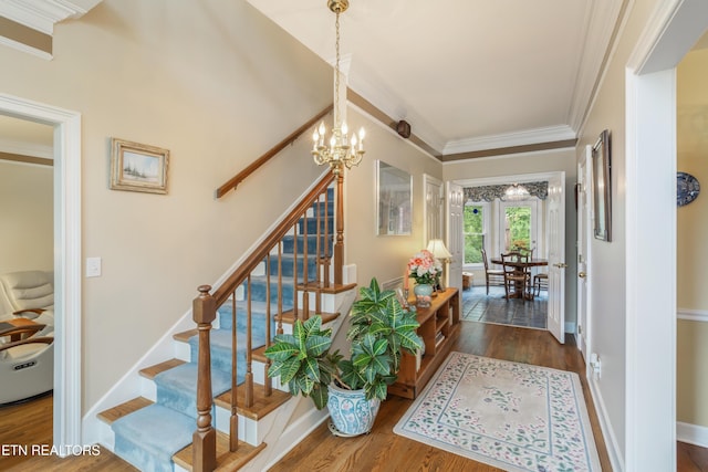 stairs with baseboards, an inviting chandelier, ornamental molding, and wood finished floors