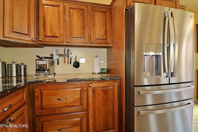 kitchen featuring brown cabinetry, dark stone counters, and stainless steel fridge