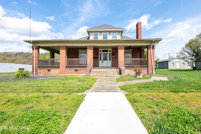 view of front of home featuring a chimney, covered porch, a front yard, and brick siding