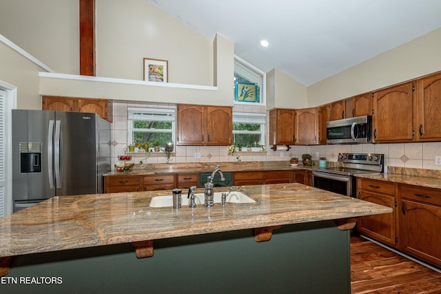 4225 W Lakeview Cir, Louisville, TN 37777 - kitchen featuring appliances with stainless steel finishes, high vaulted ceiling, brown cabinetry, a kitchen island with sink, and a sink