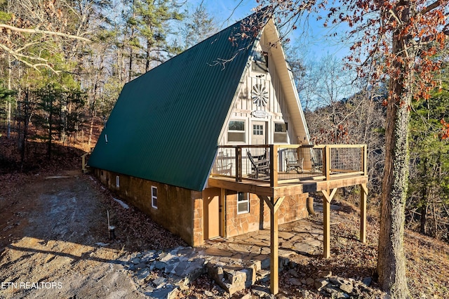 view of side of home with a wooden deck, metal roof, and stone siding