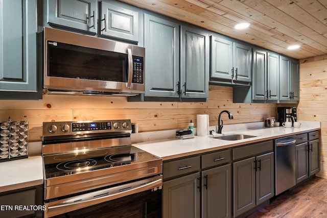 kitchen with light countertops, wood walls, stainless steel appliances, a sink, and wood finished floors