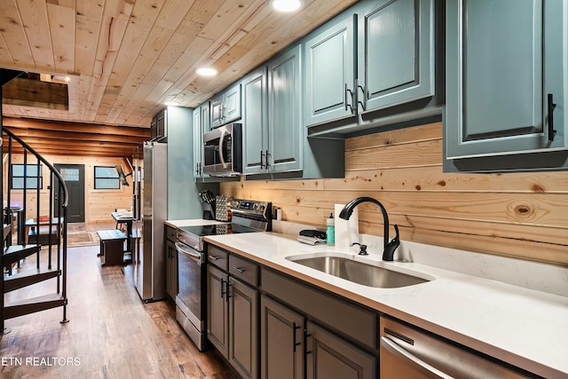 kitchen featuring a sink, light wood-style flooring, wood walls, stainless steel appliances, and wooden ceiling
