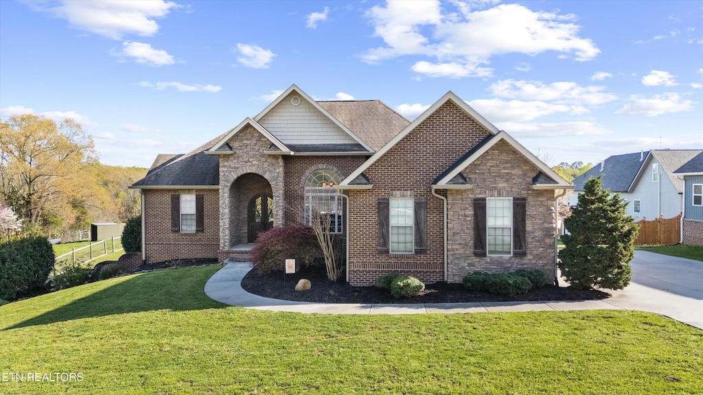 view of front of house featuring fence, a front lawn, brick siding, and stone siding