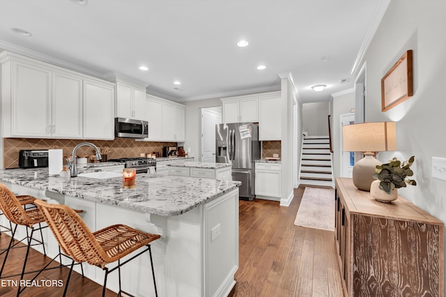 kitchen featuring a breakfast bar area, appliances with stainless steel finishes, white cabinetry, a peninsula, and ornamental molding