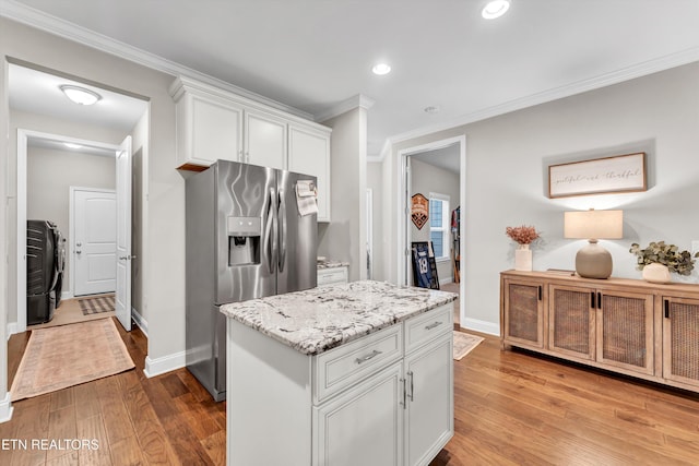 kitchen featuring white cabinets, wood finished floors, ornamental molding, light stone countertops, and stainless steel fridge
