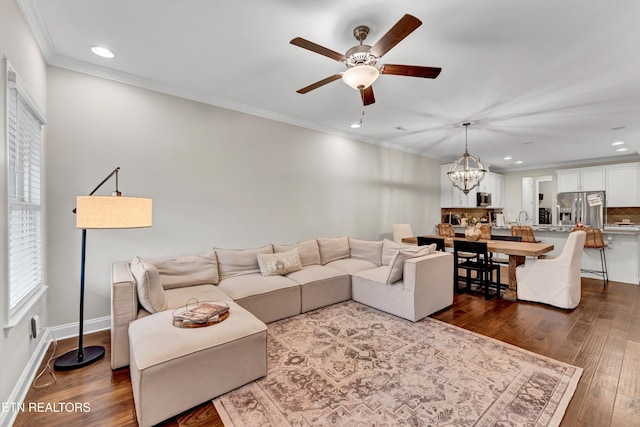 living area featuring crown molding, dark wood-style flooring, ceiling fan with notable chandelier, and recessed lighting