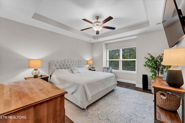 bedroom featuring ceiling fan, wood finished floors, baseboards, and a raised ceiling