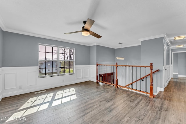 spare room featuring ceiling fan, crown molding, a wainscoted wall, and wood finished floors