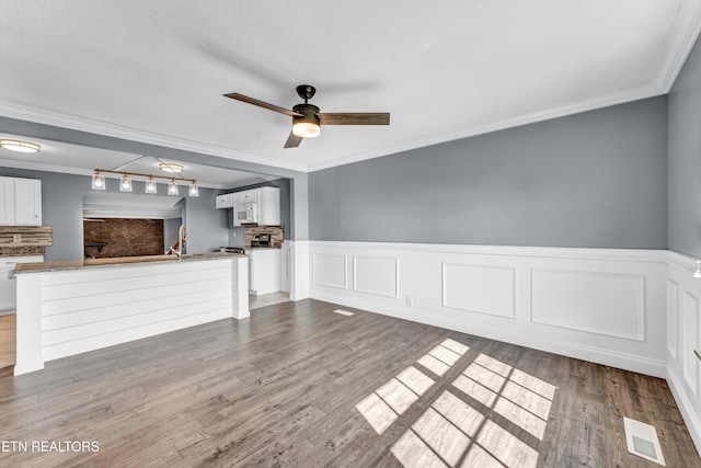 unfurnished living room featuring visible vents, track lighting, ornamental molding, ceiling fan, and dark wood finished floors