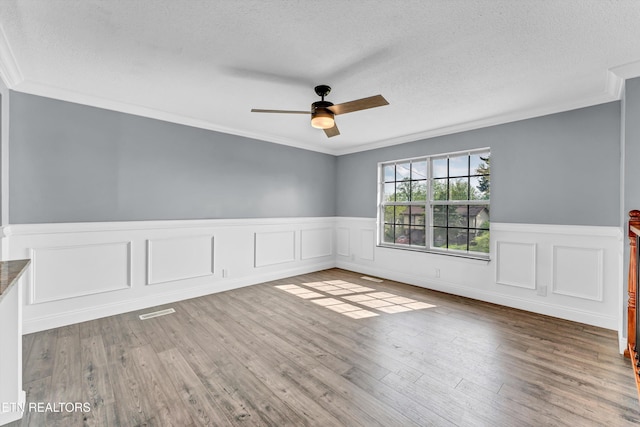 spare room with a textured ceiling, wood finished floors, crown molding, and ceiling fan