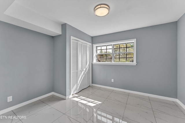 unfurnished bedroom featuring a closet, baseboards, and marble finish floor