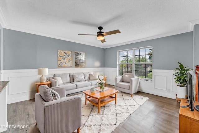 living room featuring a ceiling fan, wainscoting, wood finished floors, and a textured ceiling